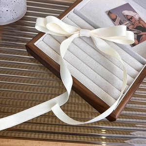 Detalle de horquilla de lazo de seda crema con borlas largas en una caja de madera