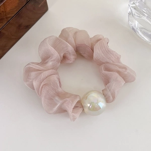 Detail of light pink organza scrunchie featuring a large iridescent pearl on a white surface