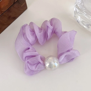 Detailed shot of a lilac satin scrunchie with large iridescent pearl on light surface
