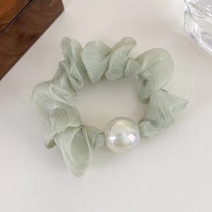 Close-up of a light green scrunchie with textured fabric and iridescent pearl detail