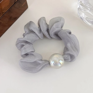 Close-up of a grey silk-feel scrunchie with a large iridescent pearl on marble background