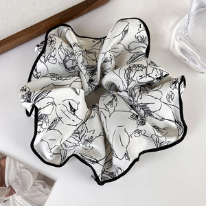 Detailed close-up of large cream satin scrunchie with elegant black floral line art