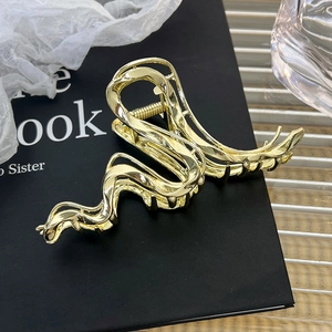 Close-up of golden wave-shaped metal hair claw with high-gloss polished texture