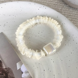 Dettaglio di elastico in organza velata con ciondolo perlato su piatto di ceramica