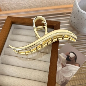 Detailed view of a gold wavy metal hair claw clip displayed on a wooden jewelry tray
