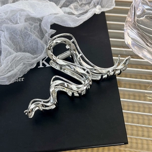 Detail of silver liquid metal hair claw clip with irregular wavy lines on a black box