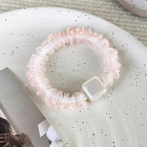 Dettaglio dello scrunchie in organza rosa con un ciondolo quadrato in resina perlata