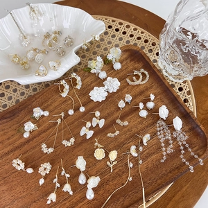 Floral shell and pearl earrings collection with tassel accents on a rustic wooden tray