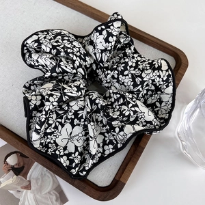 Close-up of vintage black fabric hair scrunchie with white floral pattern on a wood tray