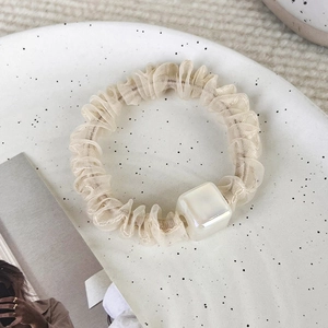 Dettaglio dell'elastico in organza beige con perla quadrata su un piatto di ceramica bianca