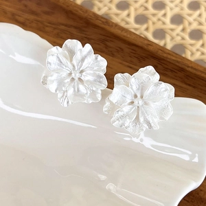 Detail macro of silver floral petal earrings with matte finish on a white ceramic plate
