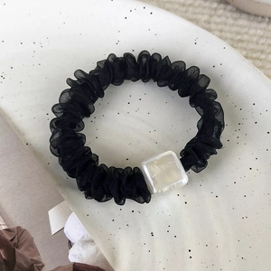 Dettaglio scrunchie in organza nera con perla quadrata in madreperla su un vassoio