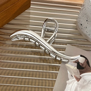 Close-up of a large silver metal claw clip with polished finish on a glass tray