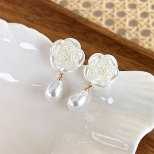 Close-up of elegant camellia floral earrings with pearl drops on a shell tray