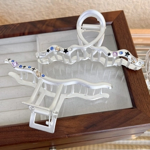 Detail of silver matte shark clip with colorful rhinestones and black stars in a wooden box