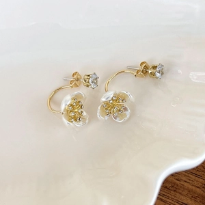 Detail of elegant gold earrings with white flower petals and crystal studs on a ceramic tray