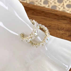Detailed macro view of gold hoop earrings with white shell flower clusters on white porcelain