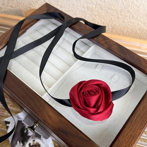 Detail of red satin 3D rose choker with long black ribbons on a vintage wooden jewelry box