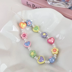 Détail d'une dragonne de téléphone en perles de cœur macaron sur un plat en céramique