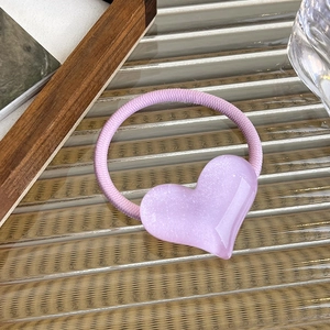 Detailed view of a light purple resin heart hair tie with glitter on fluted glass surface