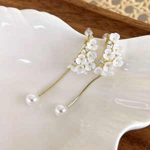 Detailed close-up of floral drop earrings with gold chain tassels and pearls on a white plate