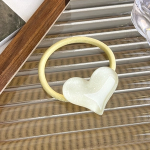 Macro view of elastic hair tie with translucent cream heart charm on textured glass