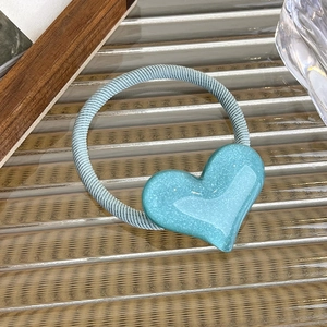 Close-up of heart ornament on light blue elastic hair tie with subtle glitter and glossy finish