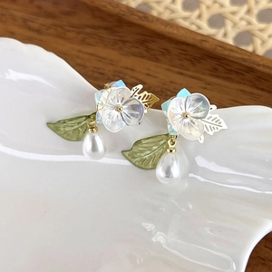 Close-up of floral drop earrings with shell petals and pearl on a white ceramic tray
