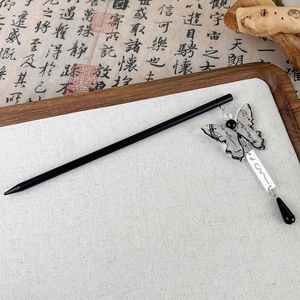 Detalle de horquilla de mariposa con patrones de caligrafía y flecos negros en bandeja