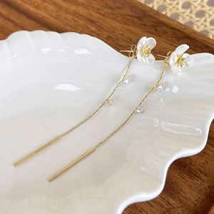 Detailed close-up of long floral drop earrings with white petals and gold tassels