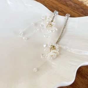 Detail of floral earrings with long diamond-set chains and resin petals on a white plate
