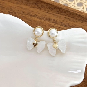 Detail of elegant gold flower earrings with white pearls and resin bow on ceramic plate