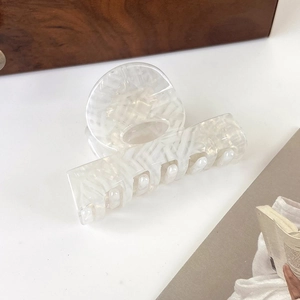 Detail of translucent cream acetate hair claw with textured woven pattern on a wooden tray