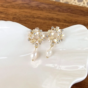 Detail of sweet flower shell earrings with pearl pendants on a white porcelain dish