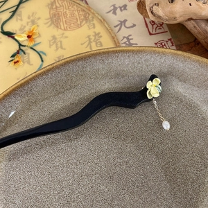 Detail of ebony wood hair stick featuring floral accents and a white pearl tassel