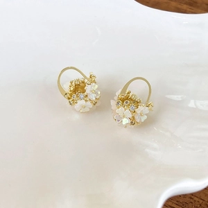 Detailed close-up of golden floral earrings with white shell petals and zircon centers