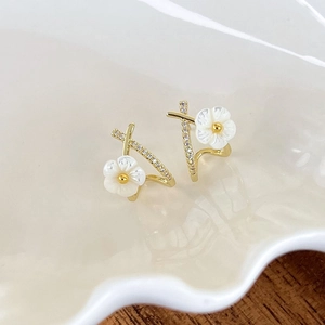 Detailed close-up of golden floral earrings with white shell petals and crystal accents