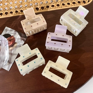 Square acetate hair claws set with rhinestones in various colors on wooden background