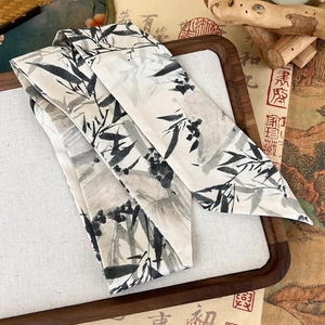 Detailed macro view of long silk ribbon scarf with ink bamboo pattern on wooden tray