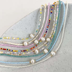 Rainbow beaded necklace set with freshwater pearls and gold beads on a ceramic plate