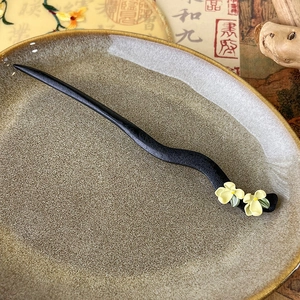 Detail of hand-carved ebony hair pin with jasmine flowers on vintage ceramic plate