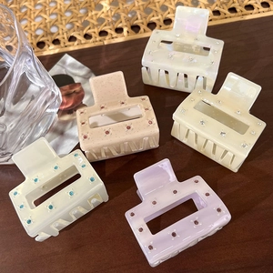 Square acetate hair claws with rhinestones in five pastel colors on a wooden table