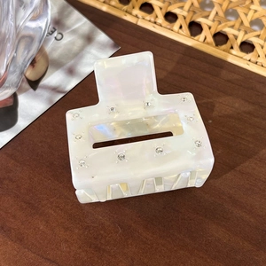 Detail of square acetate hair claw clip with white marble pattern and shiny rhinestones