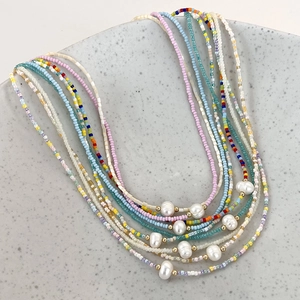 Detailed close-up of colorful seed bead necklaces with freshwater pearls in a ceramic tray