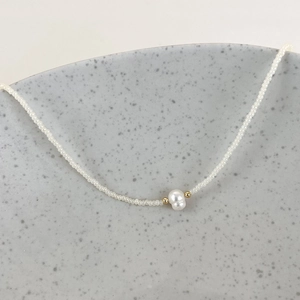 Detailed close-up of a minimalist necklace featuring a baroque pearl and white seed beads