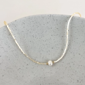 Close-up of minimalist beaded necklace with white pearls and gold accents on ceramic