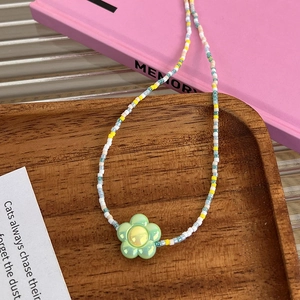 Détail d'un collier de perles colorées fait main avec pendentif fleur verte sur bois
