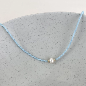 Detail of blue beaded necklace featuring a white freshwater pearl and golden accents