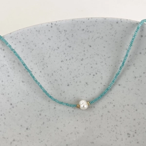 Detail view of a blue beaded necklace featuring a central pearl on a ceramic plate