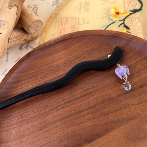 Detailed view of a purple glass lily flower pendant on a wavy wooden hair pin stick